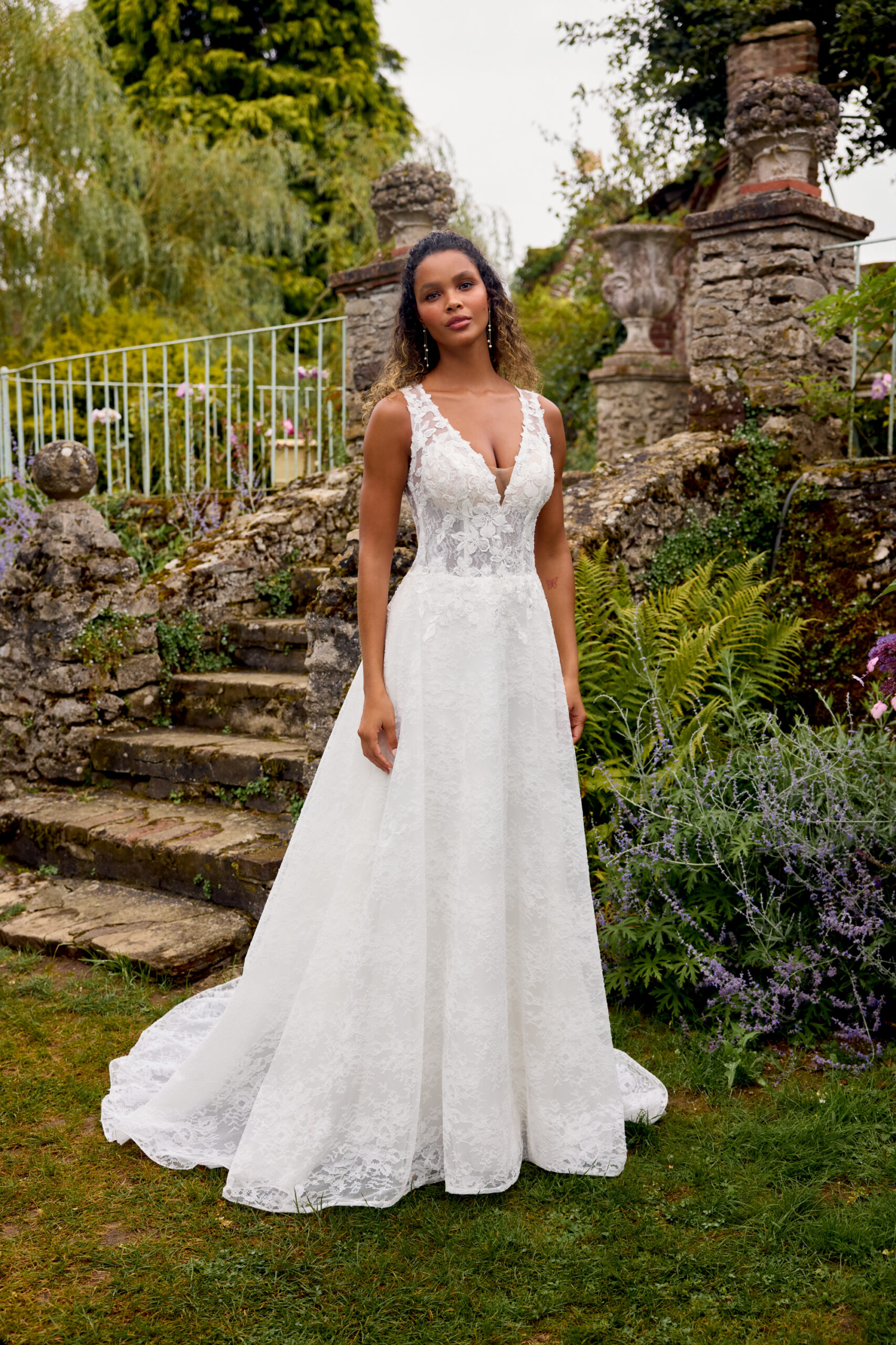 Brudklänning i helspets med A-linjeform, djup V-ringning med illusionstyll, transparent liv med pärl- och paljettbroderade spetsapplikationer, illusionrygg med knappar och svepsläp