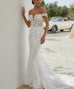 Ariana är en drömlik brudklänning i en modern fit and flare-silhuett, skapad för bruden som vill stråla med romantik och elegans. Klänningen är sydd i skimrande tyll och prydd med matta spetsapplikationer i bomull, dekorerade med handplacerade 3D-blommor som ger extra djup och rörelse. Den djupa, av axeln-skärningen tillsammans med en transparent livstycke skapar en sensuell men sofistikerad look. Baksidan avslutas med tyllklädda knappar som löper hela vägen ner till ett majestätiskt släp i chapel-längd. För dig som önskar mer täckning finns modellen även med fodrad front (modellnummer: 11350LND).