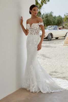 Ariana är en drömlik brudklänning i en modern fit and flare-silhuett, skapad för bruden som vill stråla med romantik och elegans. Klänningen är sydd i skimrande tyll och prydd med matta spetsapplikationer i bomull, dekorerade med handplacerade 3D-blommor som ger extra djup och rörelse. Den djupa, av axeln-skärningen tillsammans med en transparent livstycke skapar en sensuell men sofistikerad look. Baksidan avslutas med tyllklädda knappar som löper hela vägen ner till ett majestätiskt släp i chapel-längd. För dig som önskar mer täckning finns modellen även med fodrad front (modellnummer: 11350LND).